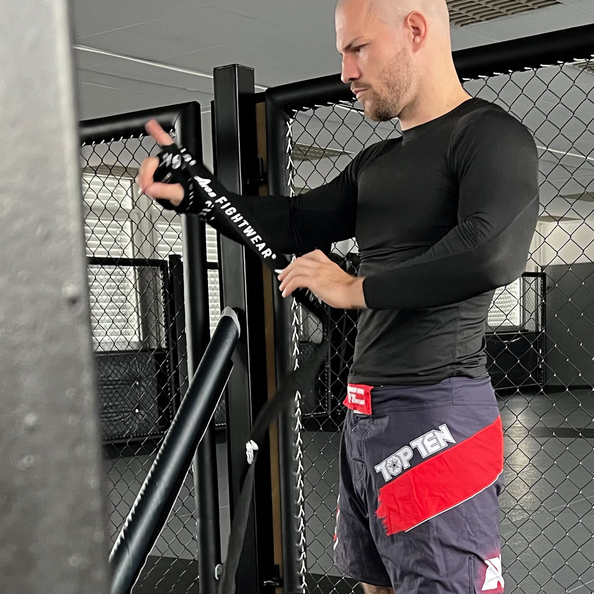 Kampfsportler bandagiert seine Hand mit Ares Fightwear Boxbandagen am Käfig